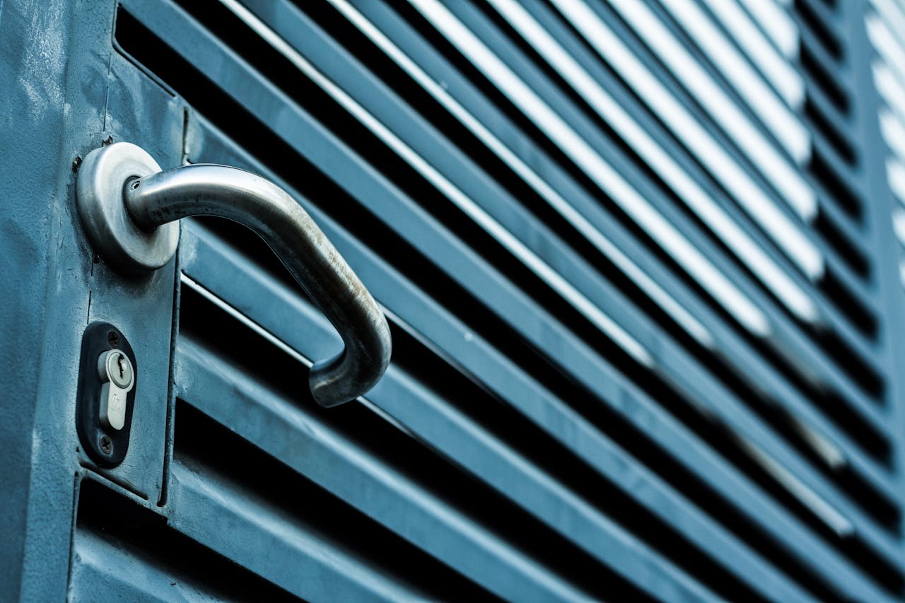 hero-img-02 Close-up of a sleek stainless steel door handle and lock on a blue metallic door.