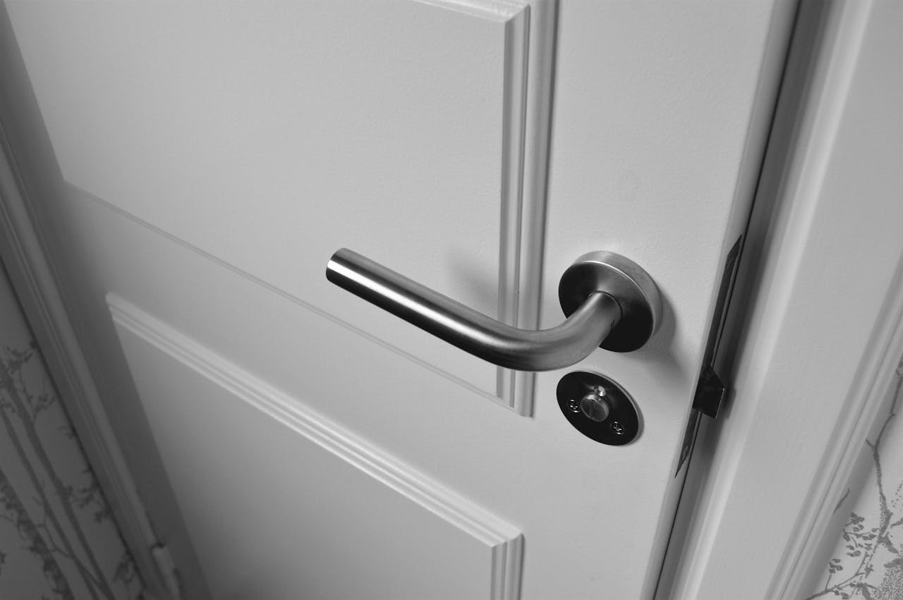 our-services-2 Close-up of a sleek steel door handle on a white door, showcasing modern interior design in monochrome.